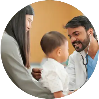 A tan middle-aged doctor uses a stethoscope on a baby as the baby sits on his mother’s lap.