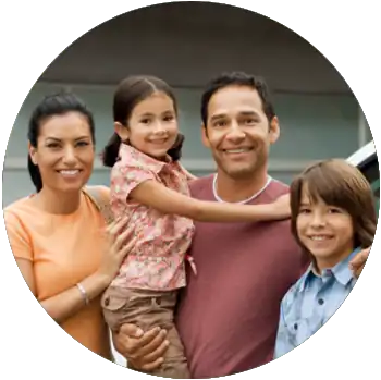A tan-skinned family is smiling and standing outside of their home and next to their car.